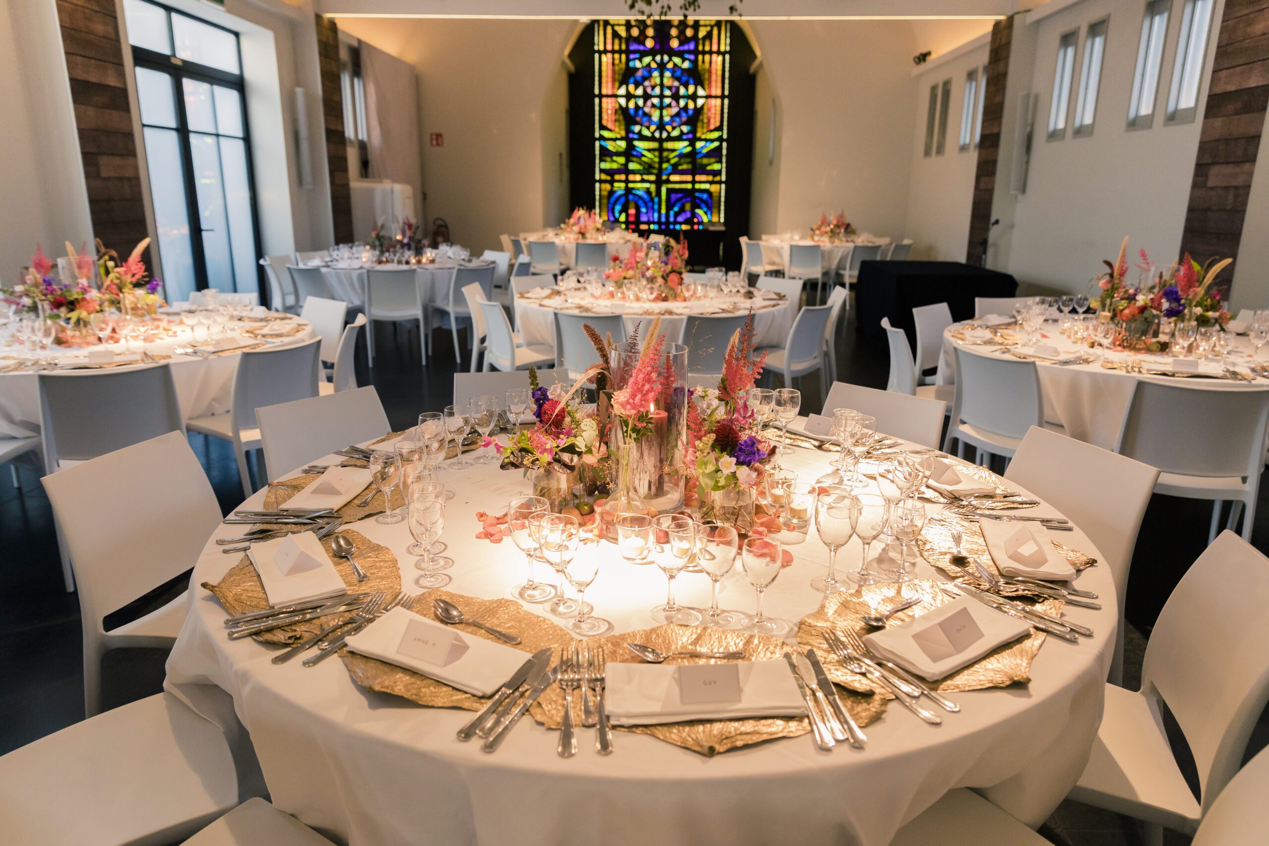 Een foto van een gedekte tafels voor het trouwfeest met heel wat glazen op en waar je de ruimte van de zaal op ziet