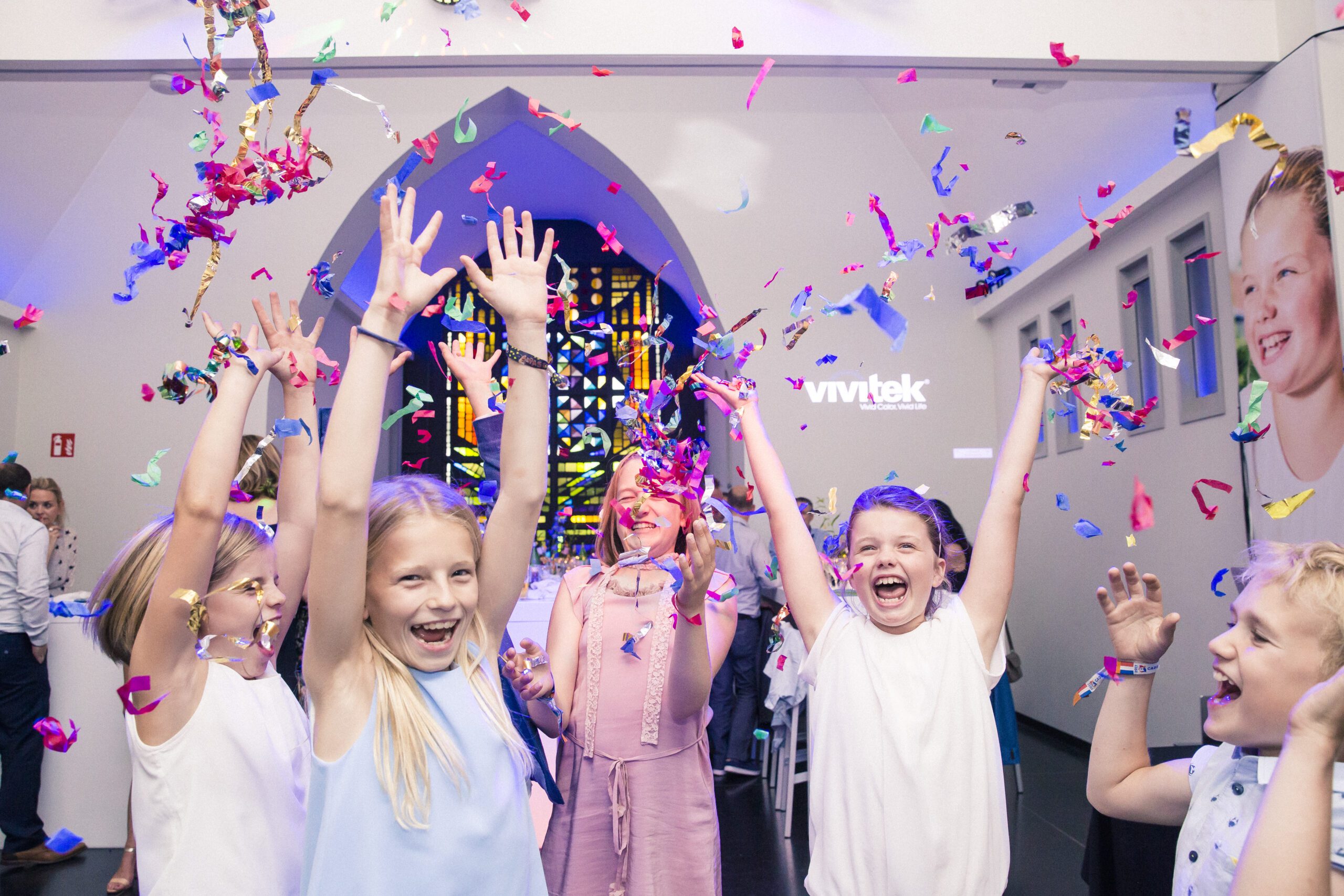 Een groepje kinderen gooit confetti omhoog op een communiefeest in De Kapel in Muizen.